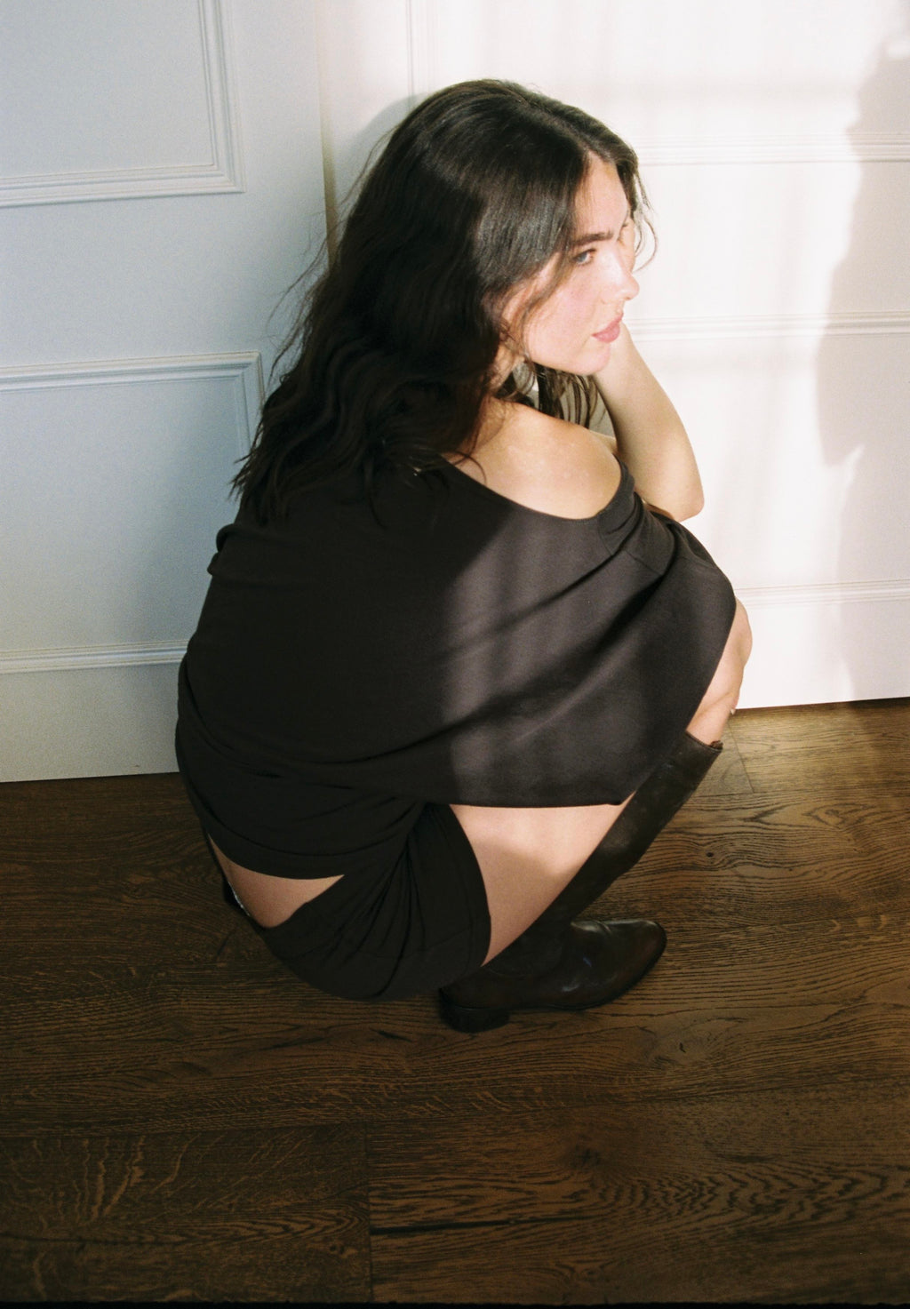 Woman sitting on a wooden floor wearing a brown dress with cut-out sides.